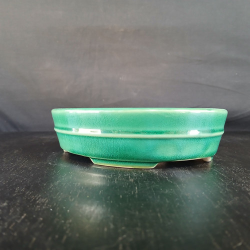 An 8-inch emerald green glazed Yixing bonsai pot sits on a dark, textured surface against a neutral black background. The pot features a glossy, vibrant finish with a subtle crackle or crazing pattern visible throughout the glaze. A prominent horizontal raised ridge encircles the center of the pot's walls, adding a classic design element to its low-profile, rounded rectangular shape. The high-quality ceramic pot is supported by small, integrated block feet that lift the base slightly. Bright highlights from an overhead light source reflect on the pot's rim and the horizontal band, accentuating its smooth, lustrous finish and rich teal-green color.