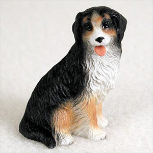 A detailed, hand-painted miniature figurine of a Bernese Mountain Dog, designed as a decorative accessory for a bonsai tree or miniature garden. The figurine depicts the dog in a classic sitting pose, looking slightly upward with a friendly and alert expression, its pink tongue playfully hanging out. 

The statue features the breed’s signature tricolor coat with a textured finish that mimics the appearance of thick fur. It has a predominantly black body and head, a stark white chest, muzzle, and paws, and warm rust-colored accents on its legs and above its eyes. The craftsmanship highlights the fine details of the dog’s face and the wavy texture of its coat, making it a charming addition for pet lovers or collectors looking to add a lifelike touch to their bonsai display.