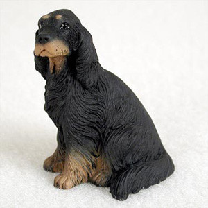 A detailed miniature figurine of a Gordon Setter dog, designed as a decorative accessory for bonsai trees. The figurine shows the dog in a sitting pose, looking alertly toward the left. It features the characteristic long, silky ears and wavy fur of the Gordon Setter breed, with a primarily black coat and tan highlights on the muzzle, paws, and distinctive "eyebrow" spots. The sculpture captures a realistic texture of the animal's coat. This small decorative statue is presented on a clean white background, highlighting its use as a charming addition to a miniature landscape or bonsai pot.