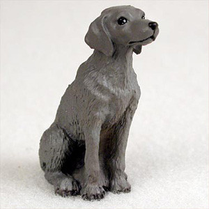 A realistic miniature Weimaraner dog figurine, crafted in a seated position and looking attentively to the right. The figurine is a solid medium grey, capturing the breed's iconic "silver" coat, with small black accents for the eyes and nose. Designed as a bonsai tree accessory or terrarium decoration, this small dog statue adds a lifelike touch and a sense of scale to miniature landscapes. The texture of the figurine subtly mimics short fur, emphasizing the elegant and athletic build of the Weimaraner breed against a plain, light background.