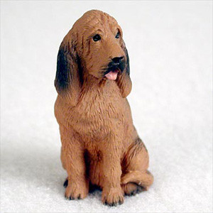 A detailed miniature figurine of a Bloodhound dog, designed as a charming decorative accessory for a bonsai tree or indoor miniature garden. The figurine captures the breed's distinctive look, featuring long, drooping ears with black-shaded tips, a wrinkled forehead, and soulful dark eyes. It is depicted in a seated position, looking slightly to the side with a small pink tongue peeking out. 

The figurine is painted in a warm, reddish-brown (liver and tan) color with dark accents on its back and ears to mimic natural fur patterns. The surface is intricately textured to represent a short, dense coat. Shown against a clean, out-of-focus white background, this small-scale Bloodhound figurine is crafted to add character and a sense of life to any bonsai arrangement or tabletop display.