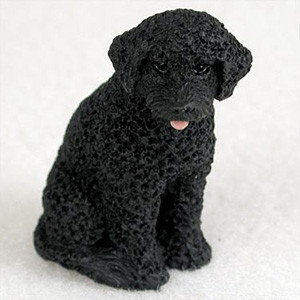 A detailed, lifelike miniature figurine of a solid black Portuguese Water Dog, specifically designed as a decorative accent for bonsai trees, terrariums, or miniature gardens. The figurine depicts the dog in a sitting pose, showcasing the characteristic thick, curly coat of the breed with a realistic, tactile texture. 

The dog’s face is finely detailed with dark, gentle eyes and a tiny pink tongue playfully peeking out from its mouth. Its ears are folded down in a soft, natural position, adding to its charming and lifelike appearance. The small scale of the statue makes it an ideal accessory for bonsai enthusiasts looking to add a personalized touch to their indoor trees or for dog lovers seeking a small collectible. The figurine is set against a plain, light-colored background that highlights the intricate craftsmanship and deep black color of the piece.