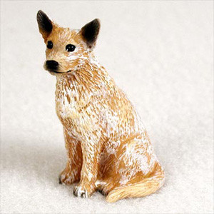 A detailed miniature figurine of a Red Australian Cattle Dog, also known as a Red Heeler, designed as a decorative accent for a bonsai tree or terrarium. The figurine is depicted in a sitting position, looking alertly toward the left. It features the breed's iconic mottled coat, with a base of reddish-tan fur intricately detailed with white speckling. 

The face has small, dark, expressive eyes, a black nose, and characteristic upright, pointed ears with black tips. The textured surface of the figurine mimics the appearance of coarse fur, highlighting its hand-painted craftsmanship. This miniature dog statue is shown against a neutral, off-white background, emphasizing its realistic features and suitability as a charming addition to a miniature garden, terrarium, or indoor bonsai tree display.