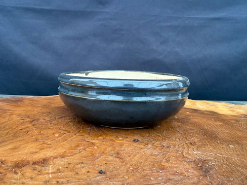 Used Andy Arnault round bonsai pot shown from the side with glossy dark black glaze, rounded body, raised rim, and light interior.