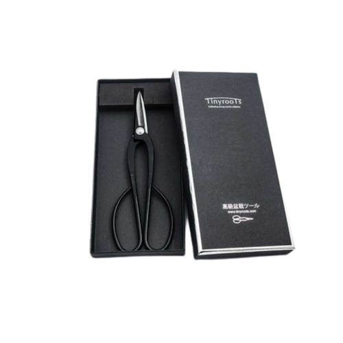 A pair of Tinyroots bowed carbon steel bonsai shears, commonly known as Ashinaga shears, displayed alongside their elegant black storage box. The long-handled shears feature a traditional design with large, rounded finger loops and sharp, pointed blades. They are resting inside a black velvet-lined tray. The accompanying black box lid is standing upright to the right, showcasing a silver border and the "Tinyroots" logo at the top. Below the logo is the slogan "Cultivating strong roots for a lifetime," and near the bottom, the box features Japanese characters that translate to "High-grade bonsai tools," the brand's website address, and a minimalist shears icon. The entire set is centered against a stark white background, highlighting the professional quality of these essential bonsai pruning tools.