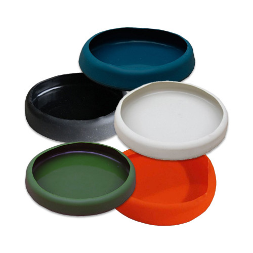 An angled, top-down photograph showcases five silicone protective bottom covers, or "boots," designed for One Leg brand stools. Arranged in an overlapping cluster against a plain white background, the covers are displayed in five distinct colors: teal blue at the top, classic black on the left, an off-white cream in the center, forest green at the bottom left, and a vibrant orange at the bottom right. 

Each circular cover features a shallow, cup-like design with a thick, rounded rim and a smooth, matte finish. These flexible silicone boots are designed to fit snugly over the base of a stool leg, providing a non-slip surface and protecting floors from scratches and scuffs while adding a decorative touch.