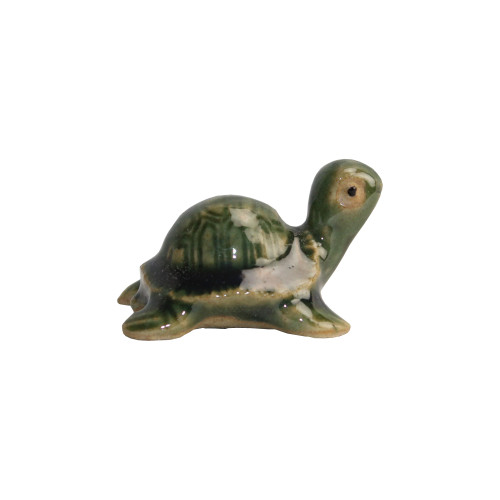 A miniature Chinese ceramic figurine of a green turtle, designed as a decorative accessory for bonsai tree landscapes. The turtle is rendered in a stylized form with a high-gloss, multi-toned glaze. Its rounded shell features a deep forest green color with vertical carved lines to mimic natural scute textures, accented by artistic patches of cream and white glaze. The turtle’s head and neck are raised in a lighter sage green hue, featuring a simple black dot for an eye. Four stubby, rounded legs peek out from beneath the shell, grounding the small figure. This charming glazed pottery piece is typical of traditional figurines used to add a sense of scale and life to miniature tray gardens and bonsai displays.
