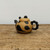 A whimsical Yixing clay teapot, designed in the likeness of a giant panda, sits centered on a rustic, light-grained wooden tabletop. The spherical body of the teapot is crafted from a natural, warm ochre-colored clay and is adorned with smooth black patches that cleverly represent a panda's distinctive eye markings and body spots. 

The lid of the teapot fits snugly and features two small, rounded black protrusions resembling panda ears. On the left side, a short, black spout angles upwards, while on the right, a thick, black C-shaped handle is decorated with a unique scalloped or gear-like outer edge. The teapot is presented against a clean, neutral off-white background with soft, even lighting that highlights the smooth, unglazed texture of the zisha clay. This handcrafted panda-themed teapot is a charming example of functional art, suitable for a traditional Chinese tea ceremony or as a decorative piece for tea enthusiasts.