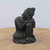 A small, weathered statue of a relaxing Buddha is featured in this image, exuding a sense of deep peace and tranquility. The dark, charcoal-gray figure, possibly made of cast resin or stone with a mossy green patina in its textured crevices, is depicted in a restful pose. His head is tilted and rests gently on his arms, which are folded over his raised left knee.

The Buddha's eyes are closed, and his face bears a serene expression, capturing a moment of quiet meditation or slumber. Traditional details are evident, including his tightly curled hair topped with a pointed ushnisha and flowing robes that drape elegantly over his body and gather around a base shaped like a stylized lotus flower.

Set against a neutral, off-white background and resting on a smooth, light-brown surface, the statue's calm presence makes it an ideal decorative accent for a Zen-inspired space or as a companion to a bonsai tree. Its aged appearance and contemplative posture evoke the timeless qualities of inner stillness and harmony central to Zen philosophy.