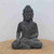 A detailed, handmade statue of a sitting Buddha, representing enlightenment and eternal knowledge, rests on a flat, light brown surface against a neutral, off-white background. The statue is crafted with a dark grey, weathered stone-like texture, featuring a matte finish. The Buddha is depicted in a traditional meditative pose with eyes closed and a serene facial expression. His hair is styled in small, uniform curls with a prominent topknot, or ushnisha, and his elongated earlobes symbolize wisdom. 

He is dressed in a flowing robe that drapes over his left shoulder, leaving the right shoulder bare, with the fabric shown in deep, rhythmic folds. His right hand reaches down toward the ground in the Bhumisparsha Mudra (the Earth Witness gesture), while his left hand rests palm-up in his lap. This Zen-inspired decorative piece is designed to bring a sense of peace and mindfulness to a garden or bonsai display.