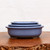 Three oval light blue glazed pots nested on a dark wood surface