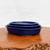 A set of three nested, oval-shaped glazed ceramic bonsai pots in a rich, vibrant cobalt blue. The pots, ranging from 10 to 15 inches in size, are stacked one inside the other, showcasing their smooth, glossy finish and classic rounded rims. The deep blue glaze has a reflective quality, catching the light against the simple, off-white background. They sit atop a textured, natural wood surface with a warm brown tone and visible grain patterns, which contrasts beautifully with the bold color of the pottery. This collection of graduated blue bonsai pots from Bonsai Outlet provides a professional and elegant option for displaying various bonsai tree species.