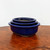 A set of three nested, oval-shaped ceramic bonsai pots with a vibrant, glossy cobalt blue glaze. The pots are stacked inside one another from largest to smallest, highlighting their uniform design and deep blue color. Each pot features a slightly flared rim with a dark, contrasting edge and a smooth, reflective surface that catches the light. The largest pot at the bottom rests on small, integrated feet, characteristic of traditional bonsai containers for drainage and aeration. They are displayed on a polished wooden surface with a rich, swirling burl-wood grain, set against a clean, neutral white background. This trio of glazed bonsai pots offers a classic and elegant choice for showcasing various bonsai tree styles.