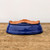 A vibrant cobalt blue glazed bonsai pot is shown upside down on a rustic, weathered wooden tabletop against a plain white background. The deep blue glaze features a glossy finish with a subtle crackle texture throughout the surface. The unglazed terracotta bottom is exposed, revealing four small pre-drilled holes designed for drainage and wiring a tree into place. This shallow pot has a smooth, curved profile and integrated scalloped feet that are part of its unglazed base. The high-quality ceramic construction and rich, deep color make it an elegant choice for displaying a variety of bonsai tree styles.