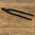 A pair of professional-grade Kaneshin No. 49 Jin Pliers, a specialized Japanese bonsai tool, rests diagonally across a weathered, light-brown wooden surface. These matte black steel pliers feature long, slender, and elegantly curved handles designed for reach and precision. The small, robust jaws at the tip are tapered and blunt, perfectly suited for delicate bonsai tasks such as peeling back bark or crushing wood fibers to create natural-looking "jin" or "shari" deadwood features. The dark finish of the high-quality tool stands out against the textured grain of the wooden tabletop, which is marked with fine scratches and indentations that suggest a well-used workshop environment.