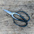A top-down, close-up photograph features a pair of Kaneshin 40E Japanese bonsai shears resting diagonally on a weathered, light-brown wooden surface. These professional-grade pruning tools, known as Ashinaga or butterfly shears, showcase a distinct design with long, slender necks and large, open-loop black handles that allow for a firm, multi-finger grip. 

The short, pointed blades are made of polished, high-carbon steel, coming together at a prominent silver pivot screw decorated with a concentric circle pattern. On the dark metal neck of one handle, delicate Japanese kanji characters are engraved, indicating the authentic craftsmanship of the Kaneshin brand. The rustic wooden background, filled with natural grain patterns, knots, and fine scratches, provides a textural contrast that highlights the clean lines and functional beauty of these traditional Japanese bonsai tools. This image captures the precision and elegance required for the meticulous art of bonsai tree shaping and maintenance.