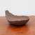An unglazed Japanese ceramic bonsai pot with a unique, organic shape, shown from a side perspective. This handcrafted planter features a deep, earthy chocolate-brown color and a matte, textured finish. Its asymmetrical form is reminiscent of a large, curled leaf or a shallow wave, with one side sweeping dramatically upwards to form a high point. The rim is delicately scalloped and irregular, adding to its rustic and natural aesthetic. The pot sits on a polished reddish-brown wooden surface, which highlights its rich tone, while the soft-white background brings focus to its artistic silhouette. This artisanal bonsai pot, identified as Japanese Planter 1512 from Bonsai Outlet, is designed for a naturalistic and expressive bonsai presentation.