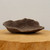 An unglazed Japanese bonsai planter with a natural, organic shape and a dark brown, earthy finish. The shallow pot features a rugged, stone-like texture and an irregular, wavy rim that mimics the appearance of a natural rock hollow. The planter is displayed on a thick, light-colored wooden pedestal against a clean, off-white background, highlighting its rustic, handmade aesthetic and wabi-sabi charm.
