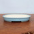 Side angle of the shallow oval pot on a textured dark wood table