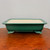 Rectangular forest green glazed pot on a polished reddish brown surface