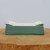 A side-view photo of a shallow, rectangular glazed ceramic bonsai pot, featured on Bonsai Outlet. The pot showcases a smooth, matte celadon green finish on its exterior walls, which contrasts with a pale, off-white interior floor where several small drainage holes are visible. The design features elegant, upward-curving "cloud" style corners on the rim and subtly flared sides. The pot is presented on a rustic, thick cross-section of a natural wood log, highlighting its earthy tones against a clean, neutral light-grey background.
