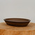 Shallow unglazed oval pot resting on a pale wood round