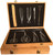 An open, light-colored bamboo storage case displays the Tinyroots Ultimate Package Stainless Steel Bonsai Tool Kit. The interior of the case features a black foam insert with custom-cut slots neatly organizing ten professional-grade bonsai tools. The set includes various polished stainless steel instruments such as long-handled pruning shears, trimming scissors, concave branch cutters, wire cutters, a root rake, and specialized tweezers. The open case rests atop a second, closed matching bamboo case, both finished with elegant brass-colored metal latches.
