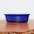 A side-profile view of a rectangular blue glazed ceramic bonsai pot, showcasing a deep, vibrant cobalt blue finish. The pot features a smooth, glossy glaze with subtle variations in color, an elegant outward-flaring top rim, and integrated small feet with decorative arched cutouts between them to provide drainage and airflow. It is displayed on a polished brown wooden surface against a minimalist white background, highlighting the pot's clean lines and rich color.