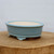 Oval light blue glazed pot on a rustic slice of natural wood