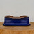 A professional, eye-level photograph showcases a rectangular 8-inch glazed bonsai pot in a rich, vibrant cobalt blue. The pot features a glossy, slightly mottled glaze on its exterior, while the upper rim and interior reveal the matte, natural reddish-brown clay. Its design is classic and elegant, with a subtle flare at the base and a decorative ridge near the top. The interior of the shallow pot shows drainage and wire holes, which are essential for healthy bonsai growth. The pot is centered on a rustic, circular wooden pedestal made from a tree trunk cross-section, set against a clean and neutral light-gray background.