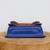 A high-quality nine-inch blue glazed bonsai pot, shown upside down to highlight its craftsmanship and functional features. The planter, available from Bonsai Outlet, features a vibrant cobalt blue glossy finish on its exterior walls, contrasting with the warm, reddish-brown unglazed clay on the bottom. Its classic rectangular design includes inward-sloping sides and a decorative raised rim. Four ornate, cloud-style feet are positioned at the corners, designed to elevate the pot for better drainage and air circulation. The bottom shows two large circular drainage holes and several smaller wire holes, essential for securing a bonsai tree. The pot sits on a thick, natural wood slice against a plain white background, emphasizing its elegant form and rich color.