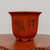 A front-facing, full shot shows a ten-inch square unglazed bonsai planter made of reddish-orange clay, featuring a flared rim and four block feet. The pot's matte surface is decorated with a detailed etched design of blooming flowers and long, slender leaves on the left, and hand-carved Chinese calligraphy on the right. Small drainage or aeration holes are clustered near the bottom corner. The planter sits on a polished, dark brown wooden stand with a natural, irregular burl edge, set against a plain, off-white background.