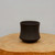 Small unglazed dark brown pot on a thick light-toned wood slice
