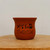 A traditional unglazed reddish-brown terracotta bonsai pot is showcased against a plain, off-white background. The pot features a classic, elegant design with a slightly flared rim and a smooth, rounded body that tapers gently towards the base. It is prominently decorated with intricate black etched Chinese calligraphy across its front. The central, larger characters read "海纳百川" (Hǎi nà bǎi chuān), a profound idiom meaning "The sea can hold the water from a hundred rivers," symbolizing great capacity, tolerance, and inclusivity. Smaller, more delicate lines of poetic script and a traditional artist's seal are etched to the left and below the main phrase. The pot sits on a rustic, light-colored wooden platform, which highlights the earthy, natural texture of the unglazed clay. Soft, even lighting creates subtle highlights on the pot's surface, emphasizing its simple yet sophisticated aesthetic.