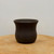 Small dark brown unglazed pot on a light-toned wooden surface
