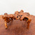 A detailed eye-level photograph showcases a natural wood root stand, model TSM1A, which is commonly used to display bonsai trees or suiseki viewing stones. The stand is expertly crafted from a gnarled and weathered root, featuring a high-gloss, varnished finish that enhances its warm amber-brown wood tones and intricate dark brown grain patterns. Its organic, irregular form is supported by four uneven legs that seamlessly transition into a knotty, interlaced top platform. This rustic and artistic display accessory is pictured resting on a large, matching polished wood surface against a plain, off-white wall, highlighting its unique textures, sculptural quality, and suitability for traditional bonsai presentation.