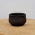 Dark charcoal unglazed pot on a light-toned wooden surface