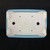 An overhead studio shot showcases the underside of a rectangular, light-blue glazed Yixing bonsai pot, set against a solid black background. The unglazed, off-white ceramic bottom is flat and functional, featuring two large circular drainage holes positioned on the left and right sides. Four smaller, precisely drilled wire holes are located near each corner, designed for anchoring a bonsai tree with training wire. In the center of the base, a square maker’s seal is embossed into the clay, featuring traditional characters that signify its origin and craftsmanship. The pot is supported by four integrated, scalloped feet at the corners, which provide elevation for proper air circulation and drainage. The outer rim of the planter displays a smooth, light blue glaze that wraps slightly around the bottom edge.