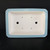 An overhead, top-down view of a rectangular Blue Yixing Planter bonsai pot, highlighting its construction and glazed finish. The pot features a wide, decorative rim and exterior walls coated in a smooth, light blue glaze, contrasting with the unglazed, off-white ceramic interior. The rectangular shape is accented by subtle, indented corners. 

Functionally, the interior base shows two large circular drainage holes positioned centrally for optimal water flow. Surrounding these are four smaller wire holes, essential for anchoring and stabilizing a bonsai tree within the pot. A small handwritten stock number, "2295 c," is visible in red ink on the right side of the inner base. The entire planter is set against a stark, solid black background to emphasize its form and color.