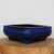 A nine-inch rectangular Yixing bonsai pot featuring a rich, glossy cobalt blue glaze. The planter has soft, rounded corners and a subtle decorative groove along its upper rim, supported by four blocky feet at each corner. It is positioned on a rustic wooden slab with visible tree rings against a clean, plain white background. The interior of the pot shows the natural, unglazed earthy brown clay typical of Yixing pottery. This deep blue glazed planter is a high-quality container designed for bonsai trees, combining traditional craftsmanship with a vibrant, eye-catching finish.