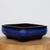 A nine-inch Yixing glazed bonsai pot in a deep cobalt blue color, featuring a dark, near-black rim. This rectangular planter has rounded corners and a slight outward curve to its walls, sitting on four sturdy, square-shaped feet. The glossy finish of the glaze reflects a soft light. The pot is presented on a natural, light-wood cross-section slab against a clean, off-white background, highlighting its artisanal quality and traditional design.
