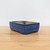 A rectangular Yixing glazed bonsai pot in a vibrant cobalt blue color, showcased on a light-colored wooden surface against a neutral white background. This high-quality ceramic bonsai container, model No. 2314H from Bonsai Outlet, features a glossy glaze with dark-edged highlights along its rims and corners, giving it a sophisticated, handcrafted appearance. The pot has a clean, rectangular silhouette with slightly rounded corners, a horizontal decorative band around its middle, and sits on four small, sturdy feet. The interior of the pot reveals a natural, unglazed tan ceramic finish, and its low-profile design is ideal for displaying a variety of bonsai tree styles.