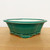 An 8-inch green glazed Yixing ceramic bonsai pot shown from a side-angle view. The pot features a vibrant teal-green glaze with a fine crackle finish, also known as crazing, which adds a vintage, textured appearance to the surface. It has a shallow, rectangular shape with rounded, scalloped corners and an elegant outward-curving rim. The container is supported by four decorative, cloud-shaped feet at the base, characteristic of traditional bonsai pottery. While the exterior is richly colored, the interior of the pot shows the natural, unglazed cream-colored ceramic. The pot is centered on a light wood-grain surface against a clean, neutral white background, emphasizing its craftsmanship and sleek design for small to medium-sized bonsai trees.