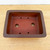 A top-down view of a 5.5-inch unglazed rectangular Yixing ceramic bonsai pot (item No. 2538) resting on a light-colored, natural wood surface. The pot features a minimalist, classic design with a deep reddish-brown terracotta color and a smooth, matte finish characteristic of high-quality, unglazed Yixing clay. 

The interior of the shallow basin reveals a practical layout for bonsai cultivation: two large circular drainage holes are centered along the middle, flanked by four smaller, precisely drilled holes near the corners intended for anchoring bonsai training wires. The pot's rim is thick with slightly rounded corners, giving it a sturdy and balanced aesthetic. This type of ceramic pot is highly valued in bonsai for its porous nature, which allows the roots to breathe and prevents waterlogging.