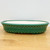 A detailed, side-profile view of a 12-inch drum-style oval Yixing ceramic bonsai pot. The pot is finished in a rich, vibrant forest green glaze that features an intricate, fine-line crackle texture. A distinctive design element is the two parallel rows of raised, circular ceramic studs or rivets circling the exterior body, giving it a classic drum-like appearance. 

The pot has a shallow, oval shape with a smooth, rounded upper rim and sits on small, integrated feet that subtly elevate it. The interior is unglazed, revealing a clean, pale cream-colored clay body. The pot is shown resting on a light-toned wooden tabletop against a plain, neutral white background, highlighting its color and craftsmanship.