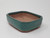 A high-quality, rectangular Yixing ceramic bonsai pot featuring a vibrant teal or seafoam green glazed exterior. The pot's design includes rounded corners with elegant decorative notches and four small, integrated feet at the base. The interior remains unglazed, showcasing the natural reddish-brown clay characteristic of authentic Yixing pottery, and includes a visible drainage hole at the bottom for plant health. This 6-inch glazed pot is photographed from an elevated three-quarter perspective against a minimalist white background, highlighting its smooth finish and classic proportions.