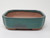 An eye-level studio photograph of a rectangular 6-inch Yixing bonsai pot centered against a clean, white background. The pot features a vibrant teal-colored glaze with a semi-glossy finish that covers the exterior walls and the top rim. Subtle variations in the glaze, such as darker, earth-toned patches near the bottom edge, give it an artisanal feel. The pot is designed with elegant notched or indented corners and slightly rounded sides. The interior and the small, integrated feet are left unglazed, revealing the natural, warm reddish-brown texture of the terracotta clay. This classic Yixing style pot is shown in a way that highlights its shape, rich color, and traditional craftsmanship.