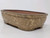 A professional studio photograph shows a 6-inch glazed Yixing bonsai pot (model YX1093B) from a three-quarter angle against a clean, white background. The rectangular pot features soft, rounded corners and a thick, rolled rim. Its exterior is finished in a high-gloss, mottled glaze with an earthy palette of olive green and warm tan, punctuated by lighter cream-colored speckles that create an organic, stone-like texture. The pot is elevated by four small, integrated block feet. The interior is unglazed, revealing the traditional, matte reddish-brown Yixing clay. The side-view perspective highlights the pot's elegant curves and the unique character of its variegated glaze.