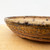 A side-view close-up of an 8.5-inch handmade round bonsai pot by ceramic artist Paul Olson. The pot features a rustic and earthy aesthetic, crafted from stoneware with a textured, ochre-colored exterior marked by deep horizontal grooves and weathered details. A thick, rounded rim is accentuated by dark-brown glaze drips that run down the sides, contrasting with the gritty, unglazed clay. Near the base, a prominent horizontal fissure adds to its unique, organic character. The planter sits on a light-colored wooden surface against a plain white background, highlighting the artisanal craftsmanship of this American-made bonsai container.