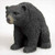 A detailed, hand-painted black bear figurine designed as a bonsai accessory. The small bear has a black body with a textured, fur-like surface and a brownish snout. It is sitting on all fours against a plain white background, looking slightly to the left with glossy black eyes, adding a realistic wildlife element to a miniature bonsai display.